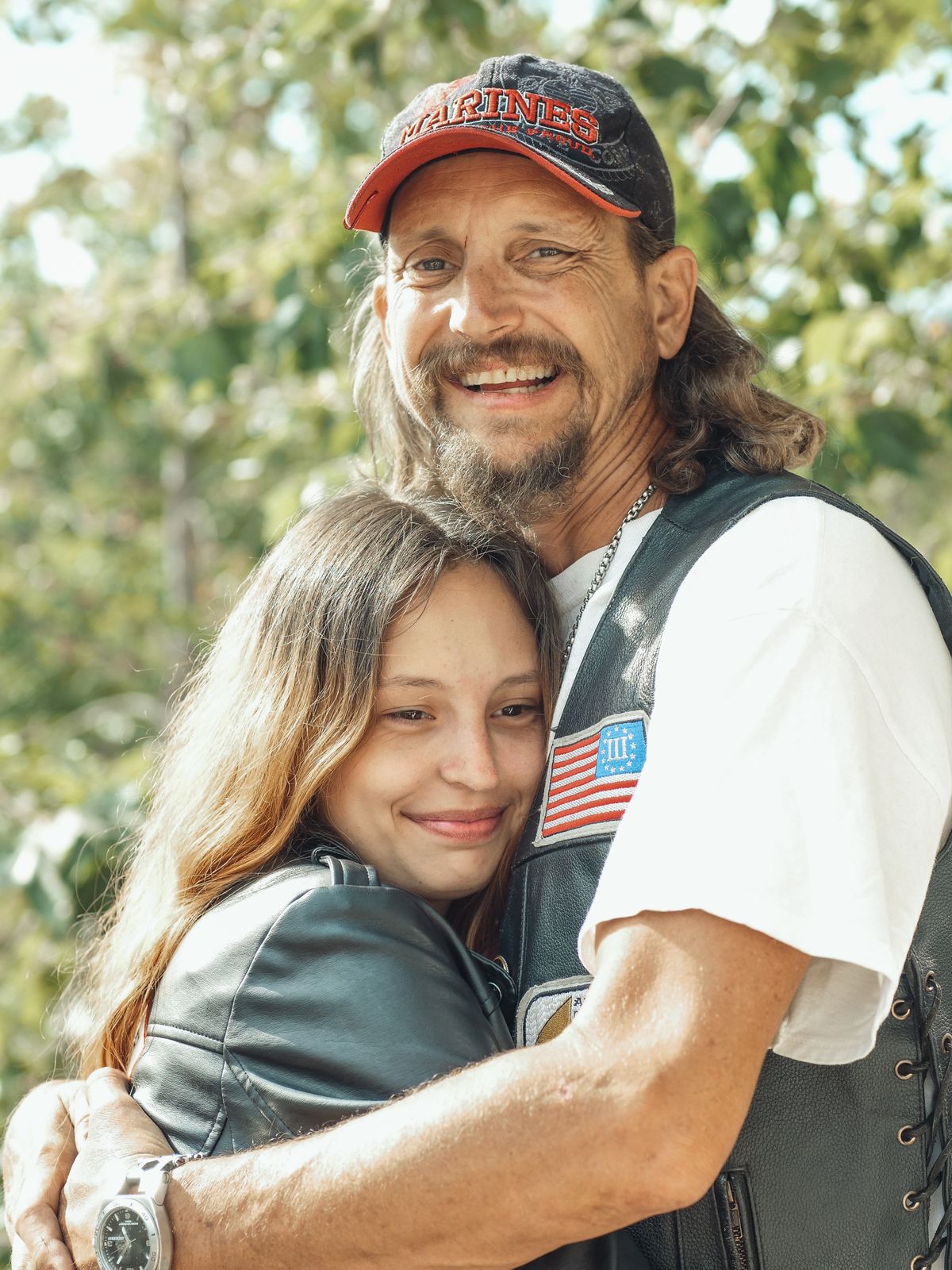 A father and daughter smiling as they embrace outdoors